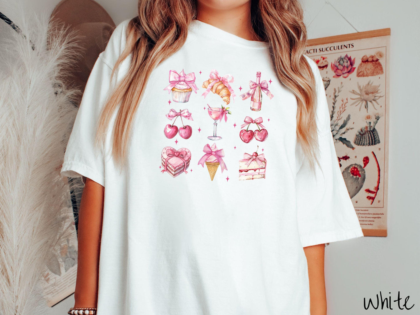 A stylish coquette Comfort Colors T-shirt featuring a grid of assorted treats with pink ribbons like a cupcake, a croissant, a champaigne bottle, cherries, a pink martini, a pink cake, and a pink ince cream cone, along with twinkling pink stars.