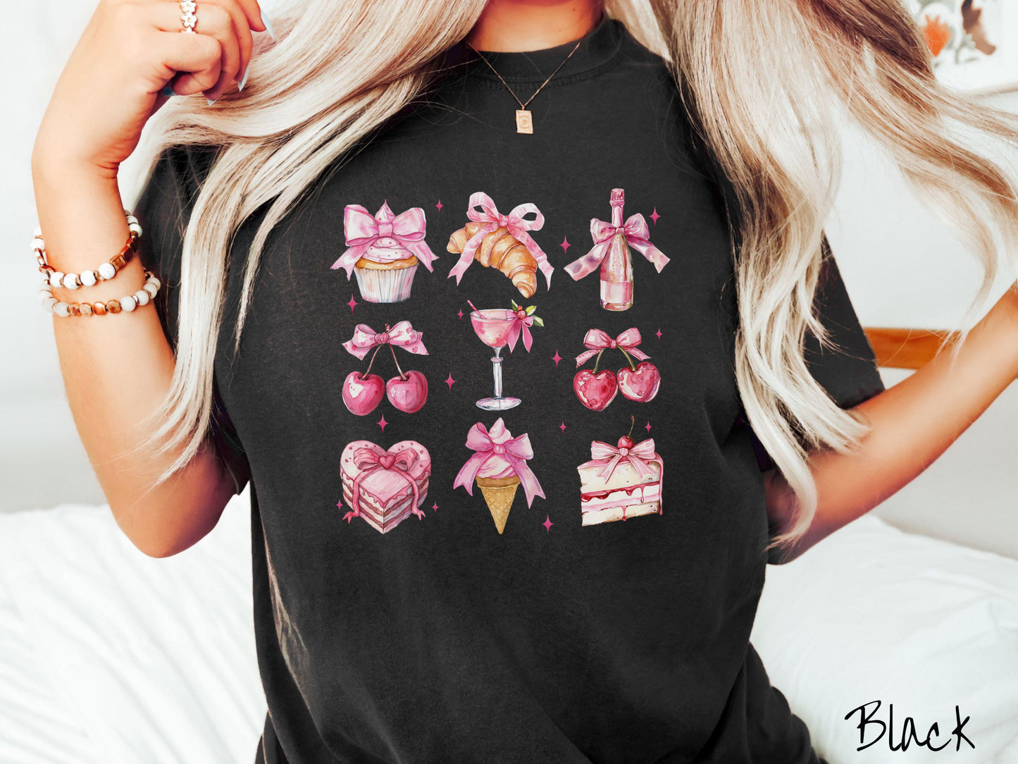 A stylish coquette Comfort Colors T-shirt featuring a grid of assorted treats with pink ribbons like a cupcake, a croissant, a champaigne bottle, cherries, a pink martini, a pink cake, and a pink ince cream cone, along with twinkling pink stars.