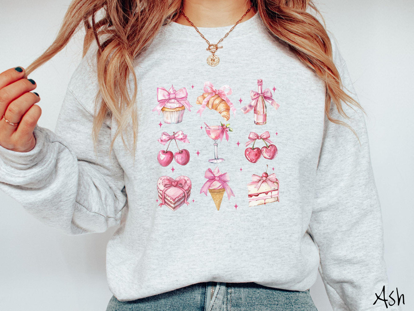 A stylish coquette Gildan sweatshirt featuring a grid of assorted treats with pink ribbons like a cupcake, a croissant, a champaigne bottle, cherries, a pink martini, a pink cake, and a pink ince cream cone, along with twinkling pink stars.