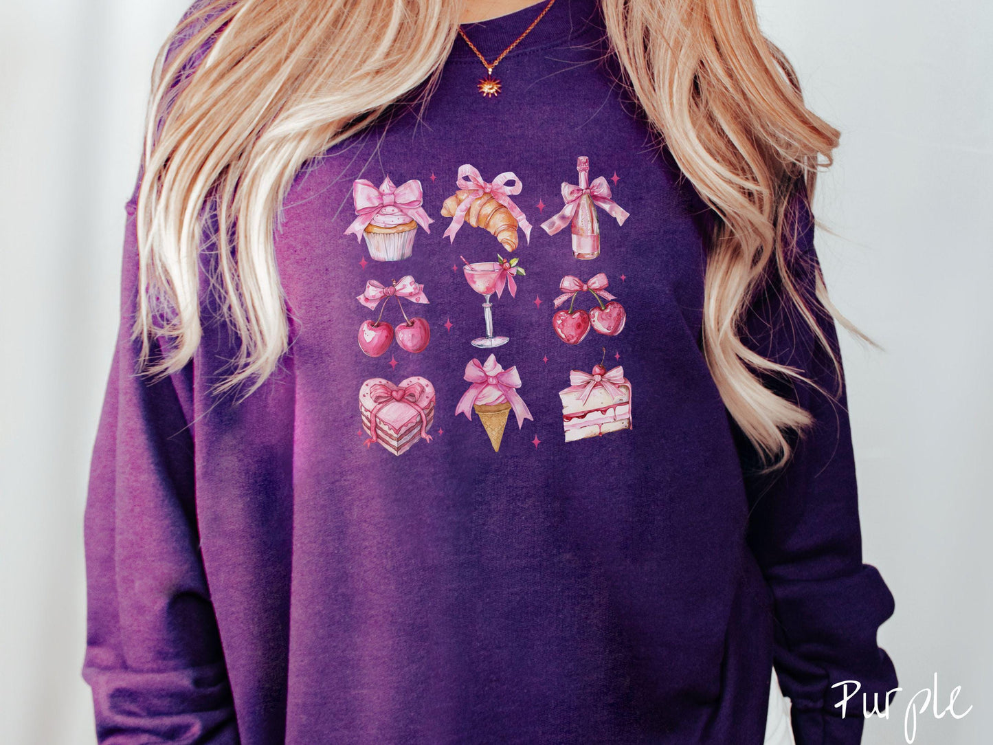 A stylish coquette Gildan sweatshirt featuring a grid of assorted treats with pink ribbons like a cupcake, a croissant, a champaigne bottle, cherries, a pink martini, a pink cake, and a pink ince cream cone, along with twinkling pink stars.