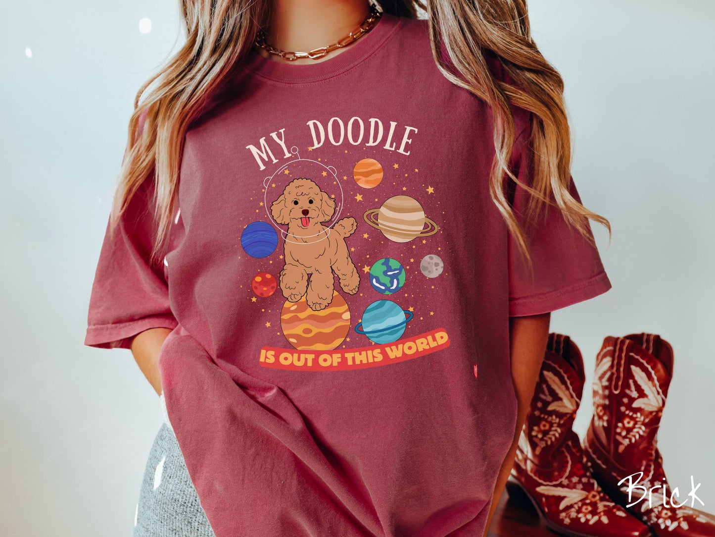 A vintage Comfort Colors t-shirt featuring the text My Doodle is Out of This World. The design showcases a Doodle sitting proudly atop Jupiter, surrounded by a vibrant solar system filled with colorful planets and twinkling stars.