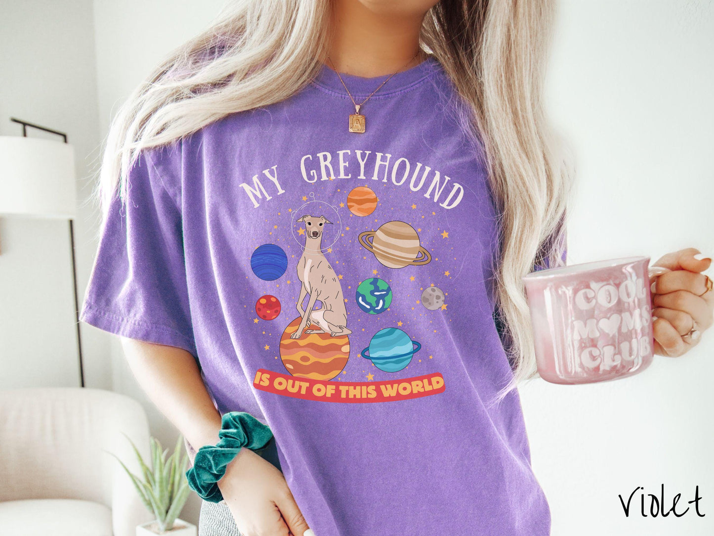 A vintage Comfort Colors t-shirt featuring the text My Greyhound is Out of This World. The design showcases a Greyhound sitting proudly atop Jupiter, surrounded by a vibrant solar system filled with colorful planets and twinkling stars.