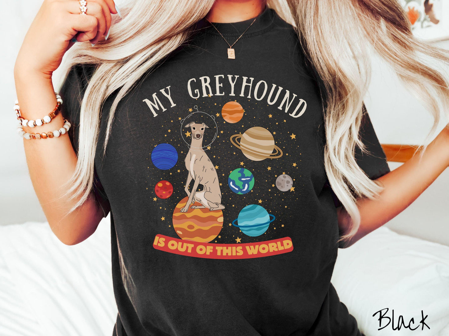 A vintage Comfort Colors t-shirt featuring the text My Greyhound is Out of This World. The design showcases a Greyhound sitting proudly atop Jupiter, surrounded by a vibrant solar system filled with colorful planets and twinkling stars.