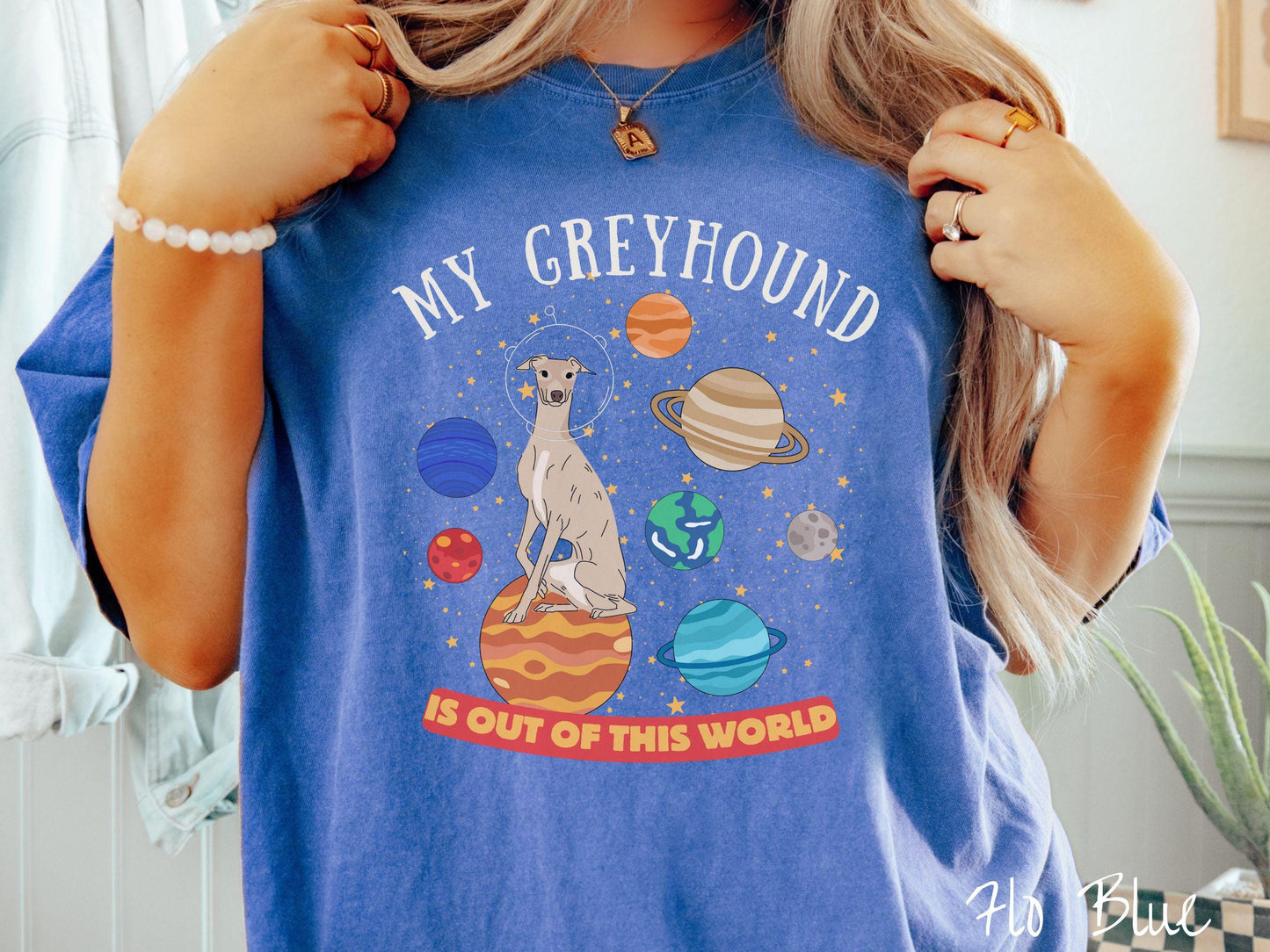 A vintage Comfort Colors t-shirt featuring the text My Greyhound is Out of This World. The design showcases a Greyhound sitting proudly atop Jupiter, surrounded by a vibrant solar system filled with colorful planets and twinkling stars.