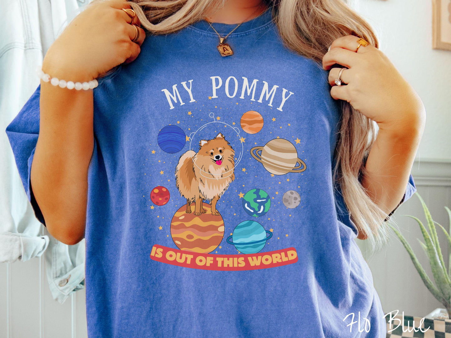 A vintage Comfort Colors t-shirt featuring the text My Pomeranian is Out of This World. The design showcases an adorable Pomeranian sitting proudly atop Jupiter, surrounded by a vibrant solar system filled with colorful planets and twinkling stars.