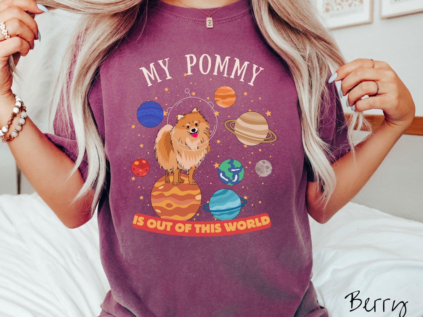 A vintage Comfort Colors t-shirt featuring the text My Pomeranian is Out of This World. The design showcases an adorable Pomeranian sitting proudly atop Jupiter, surrounded by a vibrant solar system filled with colorful planets and twinkling stars.