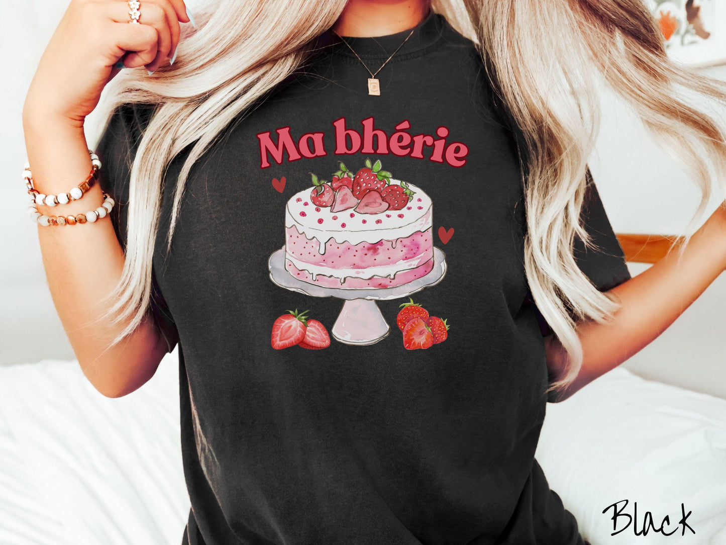 A Comfort Colors T-shirt featuring the phrase "Ma Bherie" is printed in bold red font above a charming illustration of a red-and-white strawberry cake displayed on a plate, topped with fresh strawberries and surrounded by even more berries.