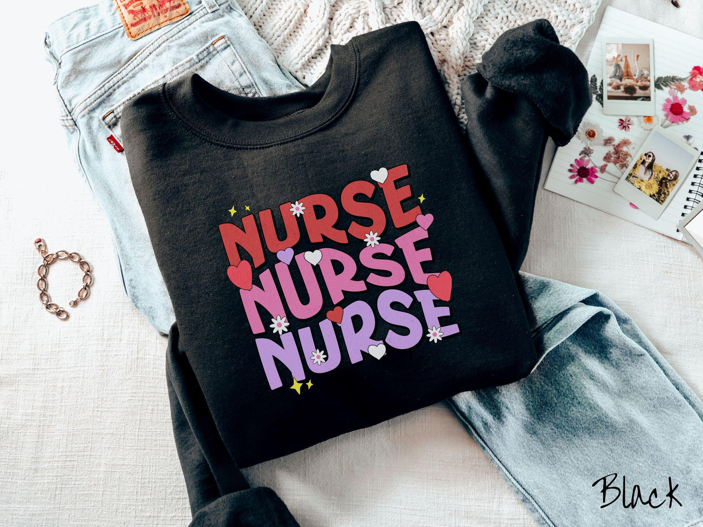 A stylish Gildan Sweatshirt featuring the word "NURSE" written three times vertically in red, pink, and purple font. There are red, white, and purple hearts mixed into the design as well as yellow twinkling stars.