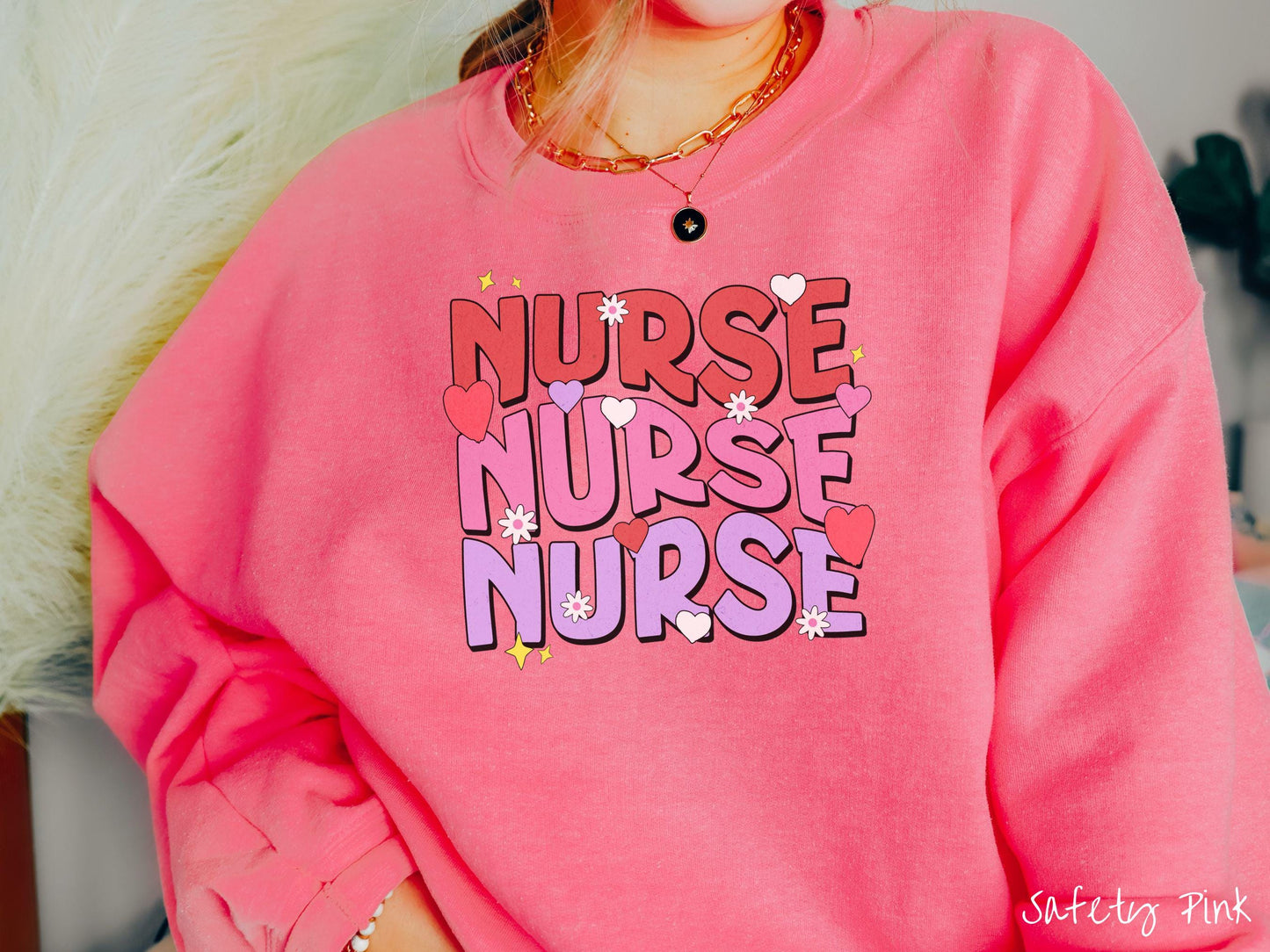 A stylish Gildan Sweatshirt featuring the word "NURSE" written three times vertically in red, pink, and purple font. There are red, white, and purple hearts mixed into the design as well as yellow twinkling stars.