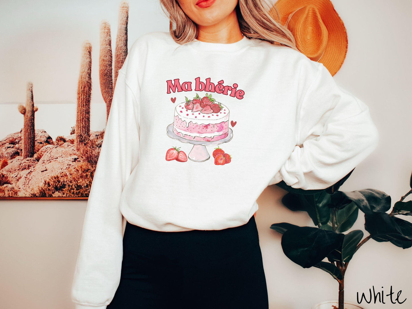 A Gildan sweatshirt featuring the phrase "Ma Bherie" is printed in bold red font above a charming illustration of a red-and-white strawberry cake displayed on a plate, topped with fresh strawberries and surrounded by even more berries.