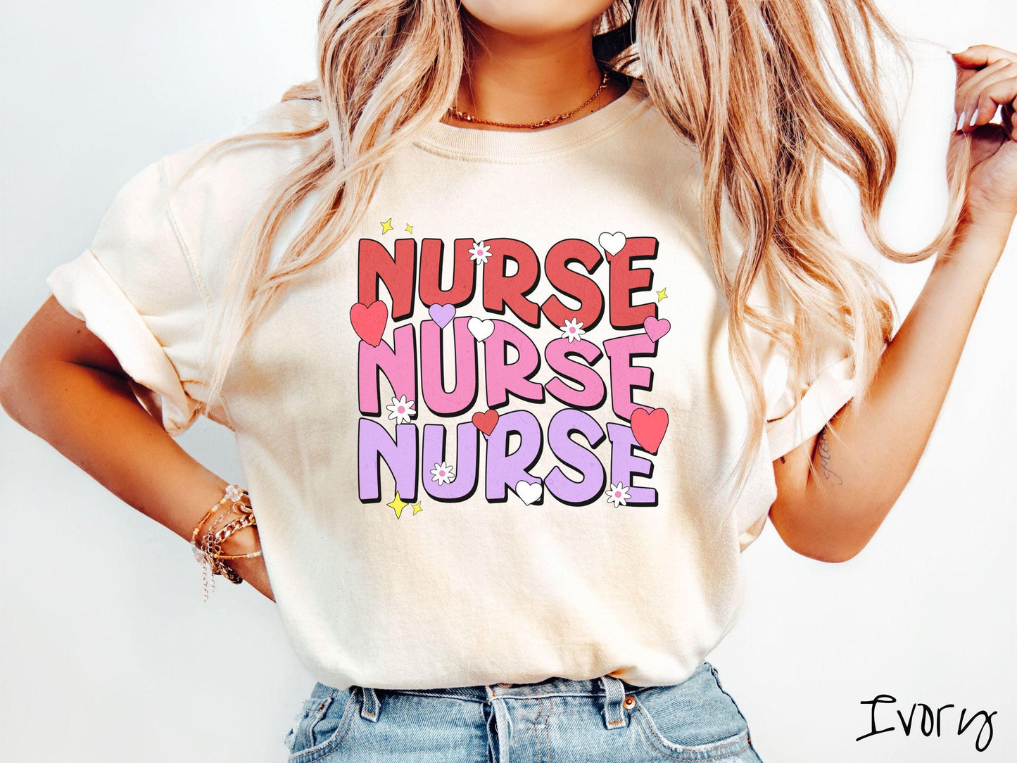 A stylish Comfort Colors T-shirt featuring the word "NURSE" written three times vertically in red, pink, and purple font. There are red, white, and purple hearts mixed into the design as well as yellow twinkling stars.