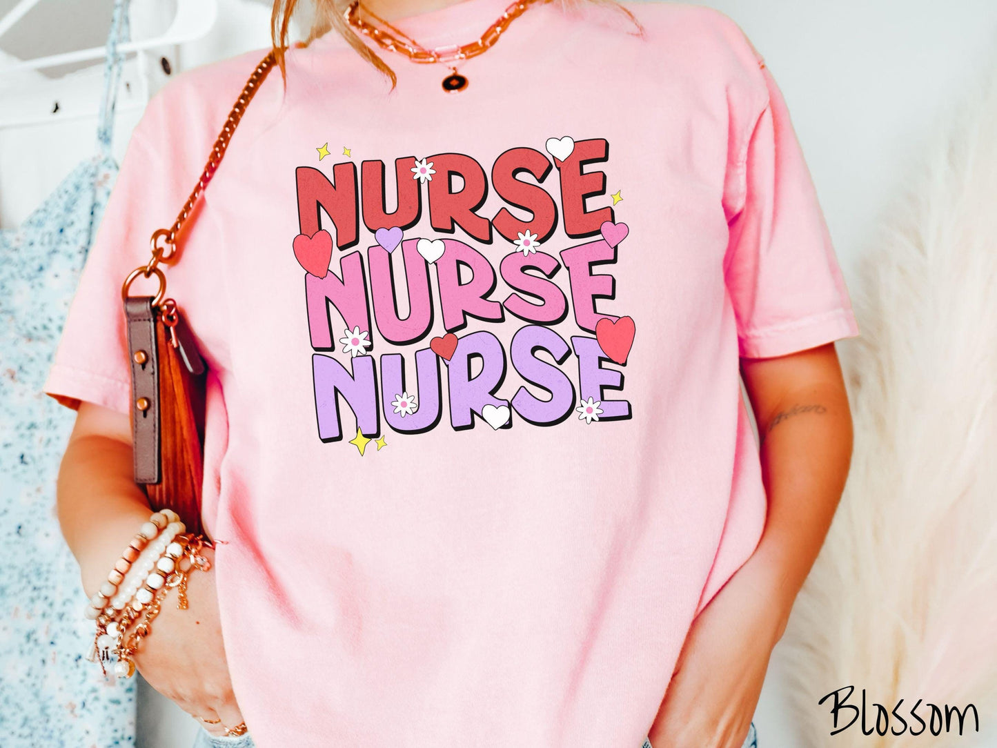 A stylish Comfort Colors T-shirt featuring the word "NURSE" written three times vertically in red, pink, and purple font. There are red, white, and purple hearts mixed into the design as well as yellow twinkling stars.