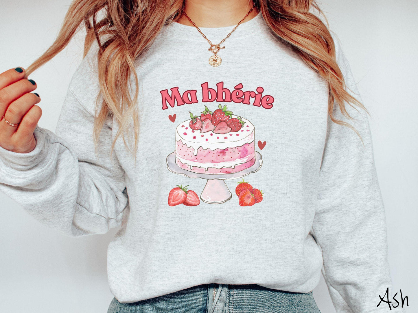A Gildan sweatshirt featuring the phrase "Ma Bherie" is printed in bold red font above a charming illustration of a red-and-white strawberry cake displayed on a plate, topped with fresh strawberries and surrounded by even more berries.