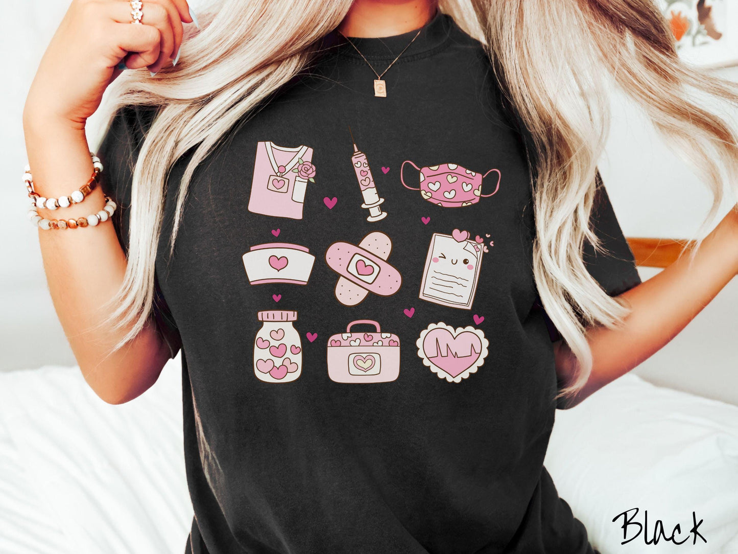 A Comfort Colors T-shirt featuring a 3x3 grid of nursing-themed illustrations adorned with heart designs like nursing scrubs, syringes, a face mask, a nurse cap, bandages, medical records, vitamins, a medical bag, and a heart-shaped EKG graph.