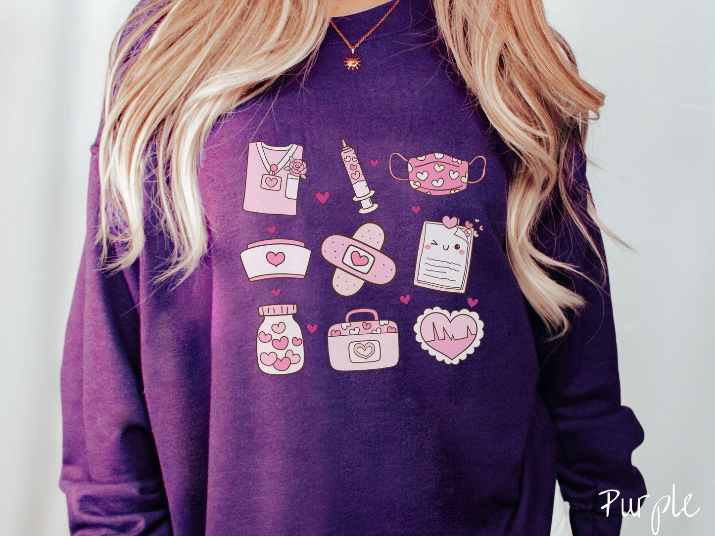 A Gildan sweatshirt featuring a 3x3 grid of nursing-themed illustrations adorned with heart designs like nursing scrubs, syringes, a face mask, a nurse cap, bandages, medical records, vitamins, a medical bag, and a heart-shaped EKG graph.