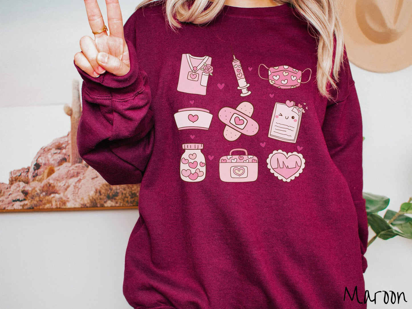 A Gildan sweatshirt featuring a 3x3 grid of nursing-themed illustrations adorned with heart designs like nursing scrubs, syringes, a face mask, a nurse cap, bandages, medical records, vitamins, a medical bag, and a heart-shaped EKG graph.