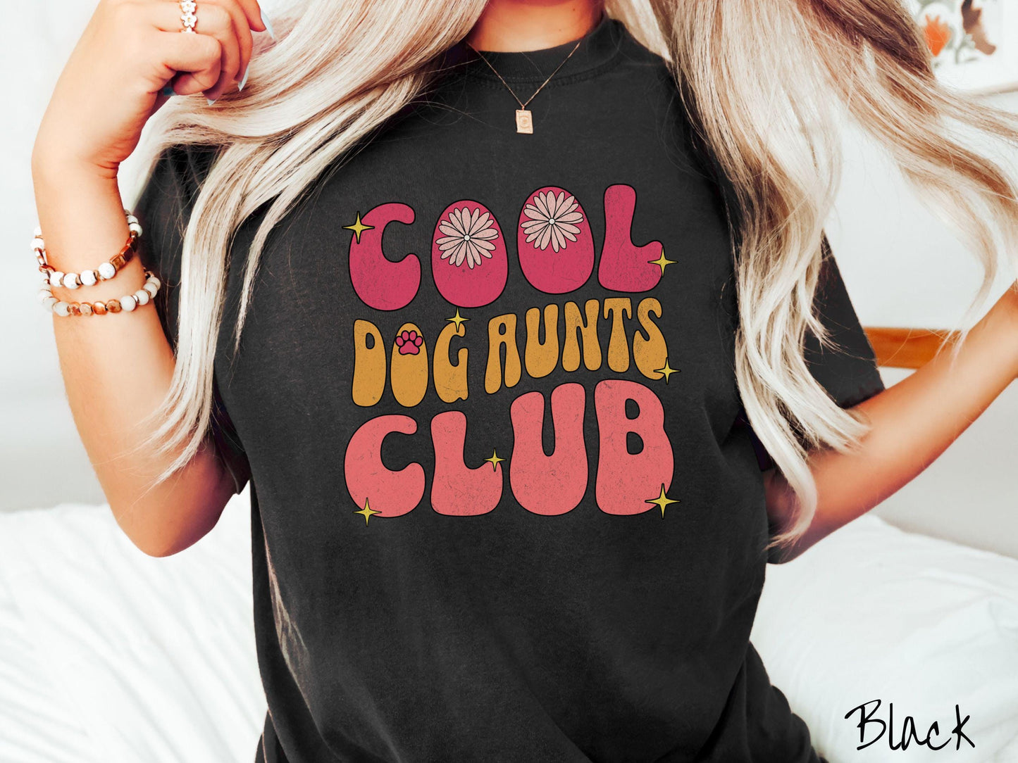 A vintage Comfort Colors t-shirt featuring the text "Cool Dog Aunts Club" in bold red, yellow, and orange fonts with flower petals nestled in the "O" of COOL, a cute red paw print in the "O" of DOG, and sparkling yellow stars throughout.
