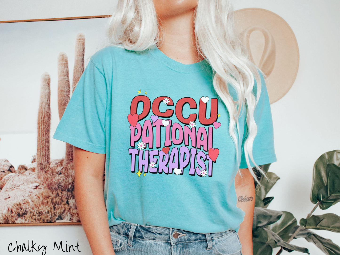 A stylish Comfort Colors t-shirt featuring the words "Occupational Therapist" arranged vertically in bold red, pink, and purple font, this design is enhanced with colorful hearts, flowers, and stars for a playful, uplifting touch.