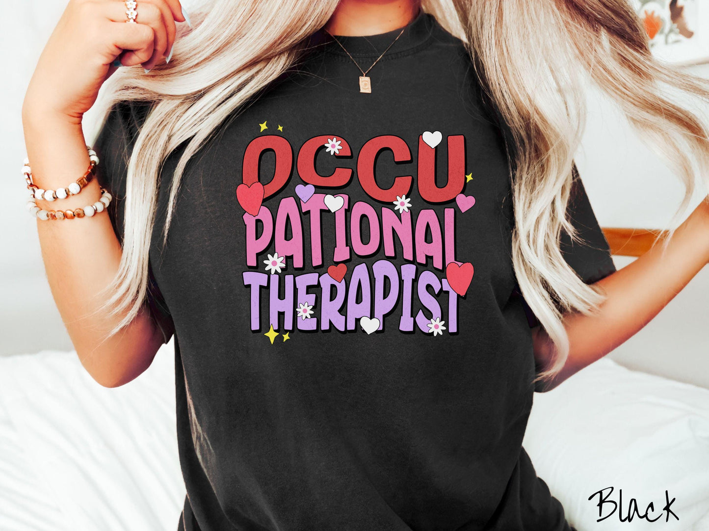 A stylish Comfort Colors t-shirt featuring the words "Occupational Therapist" arranged vertically in bold red, pink, and purple font, this design is enhanced with colorful hearts, flowers, and stars for a playful, uplifting touch.