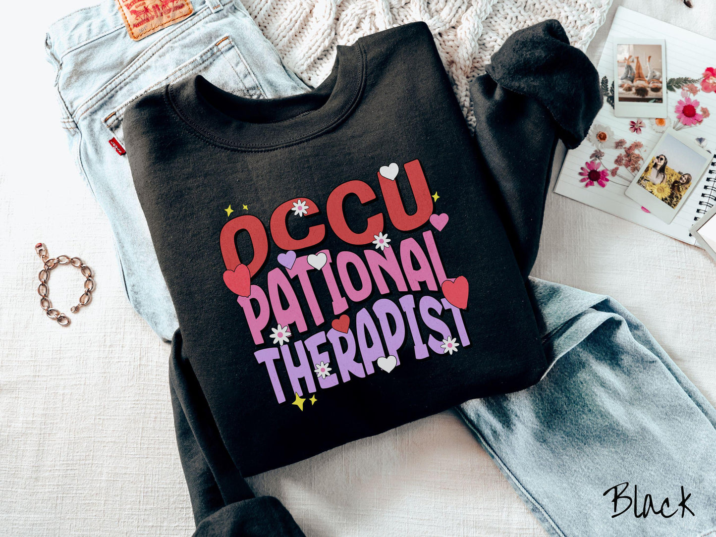 A stylish Gildan sweatshirt featuring the words "Occupational Therapist" arranged vertically in bold red, pink, and purple font, this design is enhanced with colorful hearts, flowers, and stars for a playful, uplifting touch.