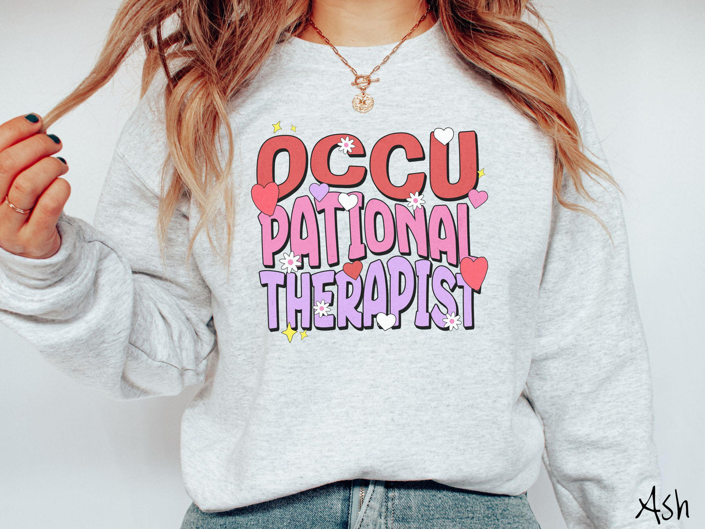 A stylish Gildan sweatshirt featuring the words "Occupational Therapist" arranged vertically in bold red, pink, and purple font, this design is enhanced with colorful hearts, flowers, and stars for a playful, uplifting touch.