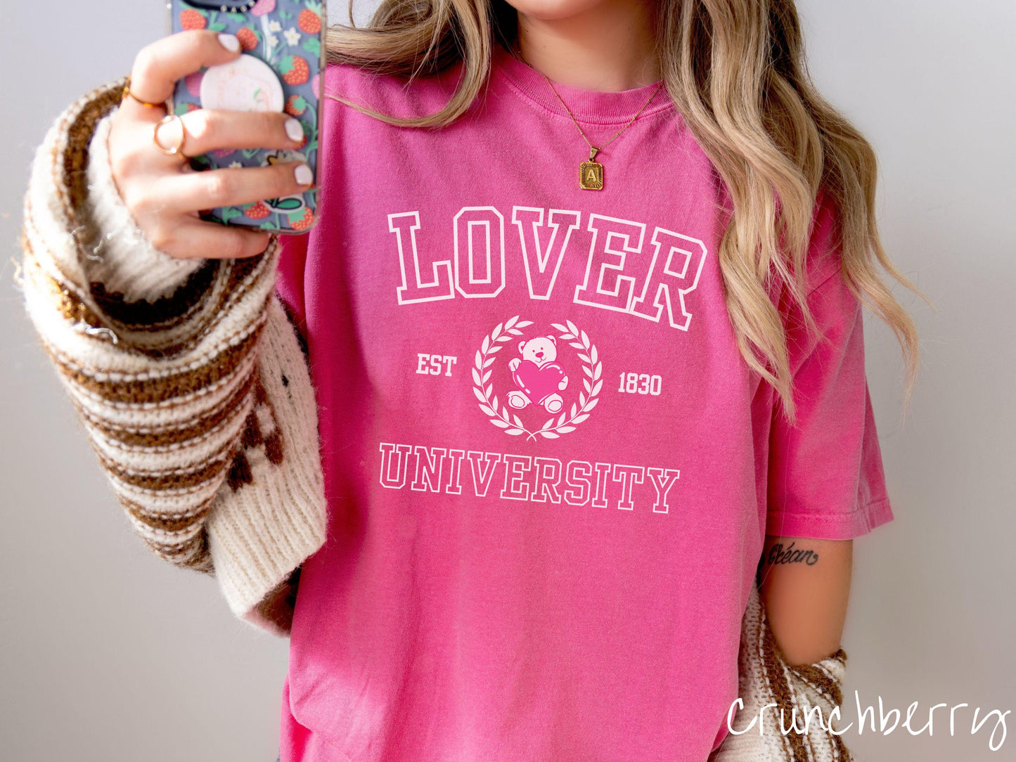 A vintage Comfort Colors t-shirt featuring a university logo-inspired design showcasing the text “Lover University” in collegiate-style font. Two pink laurel leaves frame a pink teddy bear hugging a heart with the text “EST. 1830” in pink font.