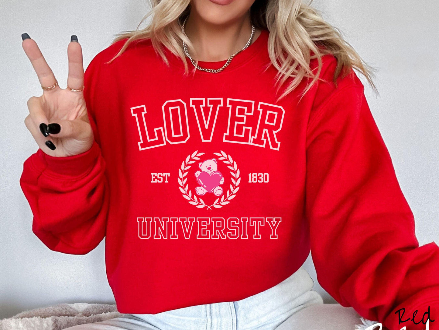 A vintage Gildan sweatshirt featuring a university logo-inspired design showcasing the text “Lover University” in collegiate-style font. Two pink laurel leaves frame a pink teddy bear hugging a heart with the text “EST. 1830” in pink font.