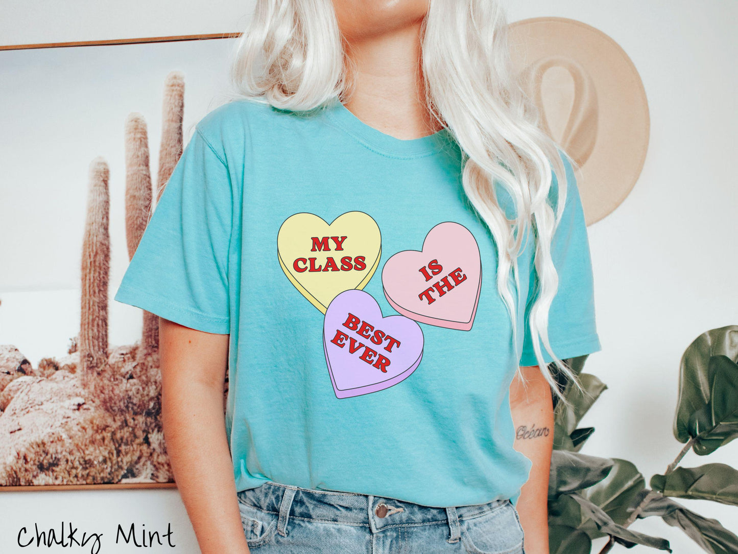 A charming vintage-style Valentine’s Day Comfort Colors t-shirt featuring three vibrant conversation hearts in yellow, red, and purple, this design displays the text “My class is the best ever” spread across the hearts.