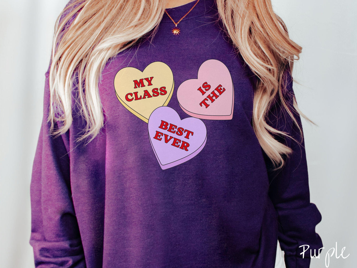 A charming vintage-style Valentine’s Day Gildan sweatshirt featuring three vibrant conversation hearts in yellow, red, and purple, this design displays the text “My class is the best ever” spread across the hearts.