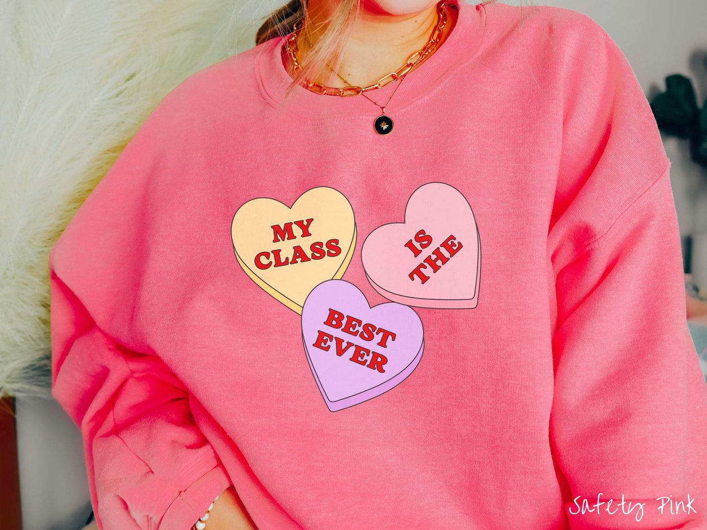 A charming vintage-style Valentine’s Day Gildan sweatshirt featuring three vibrant conversation hearts in yellow, red, and purple, this design displays the text “My class is the best ever” spread across the hearts.