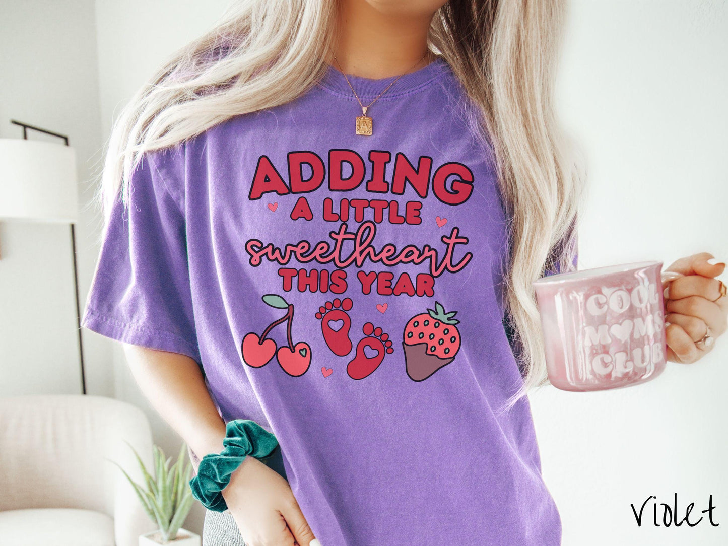 Share your exciting news with this vintage Comfort Colors t-shirt featuring the phrase “Adding a little sweetheart this year” in bold red font, paired with two red baby footprints framed by two red cherries and a chocolate-covered strawberry.
