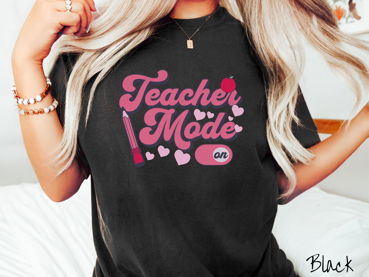 A vintage Comfort Colors t-shirt featuring the phrase “Teacher Mode” in playful pink font, an “On” button toggled to the “On” position, and with charming details like a red pencil, a red apple, and pink hearts sprinkled throughout.