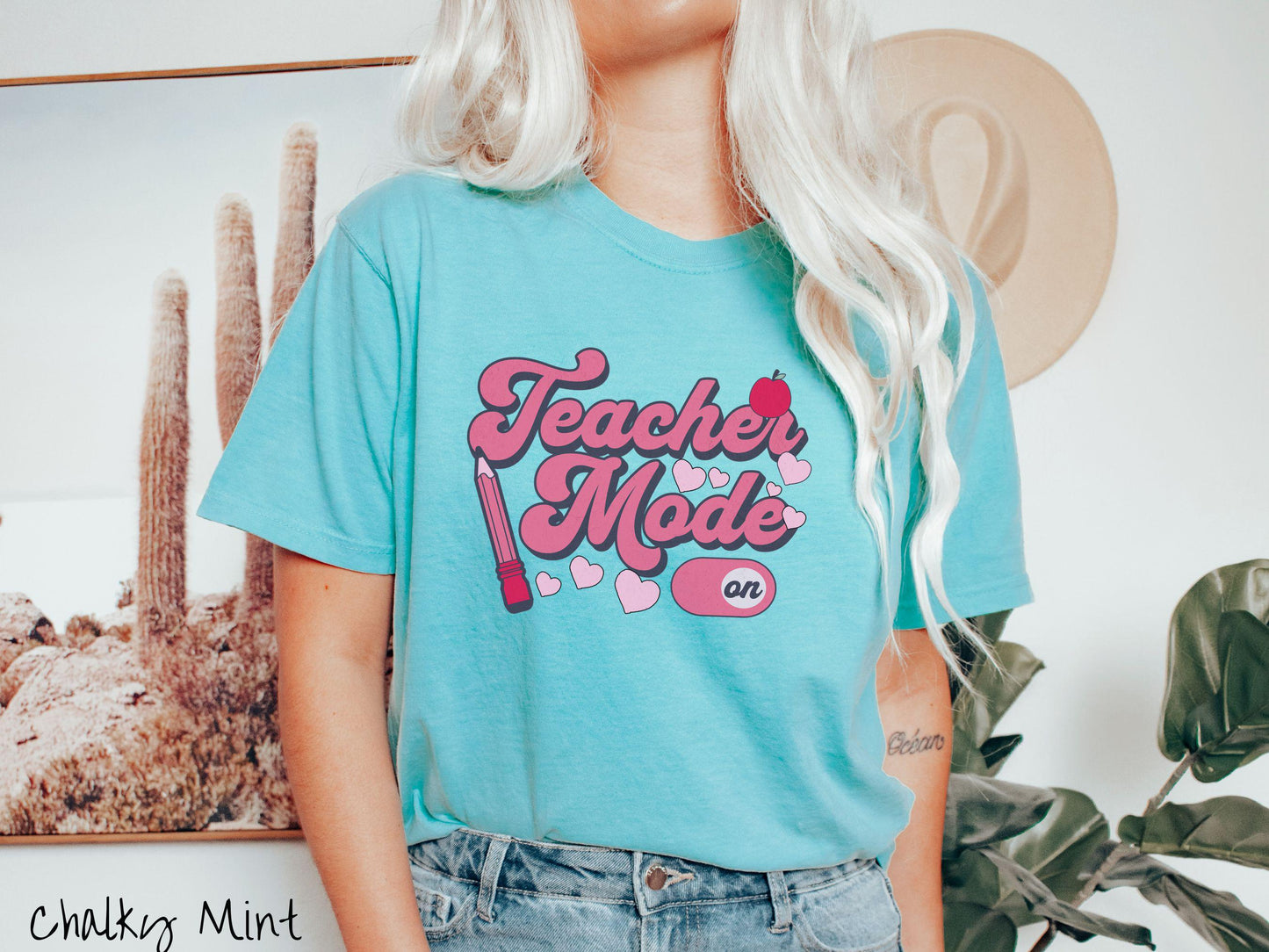 A vintage Comfort Colors t-shirt featuring the phrase “Teacher Mode” in playful pink font, an “On” button toggled to the “On” position, and with charming details like a red pencil, a red apple, and pink hearts sprinkled throughout.