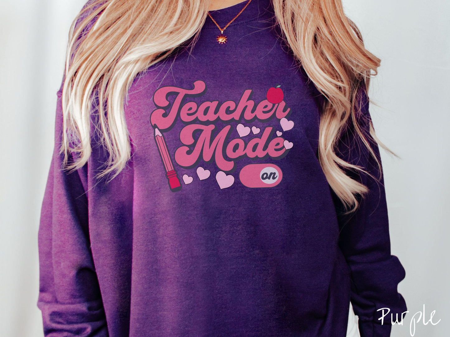 A vintage Gildan sweathirt featuring the phrase “Teacher Mode” in playful pink font, an “On” button toggled to the “On” position, and with charming details like a red pencil, a red apple, and pink hearts sprinkled throughout.