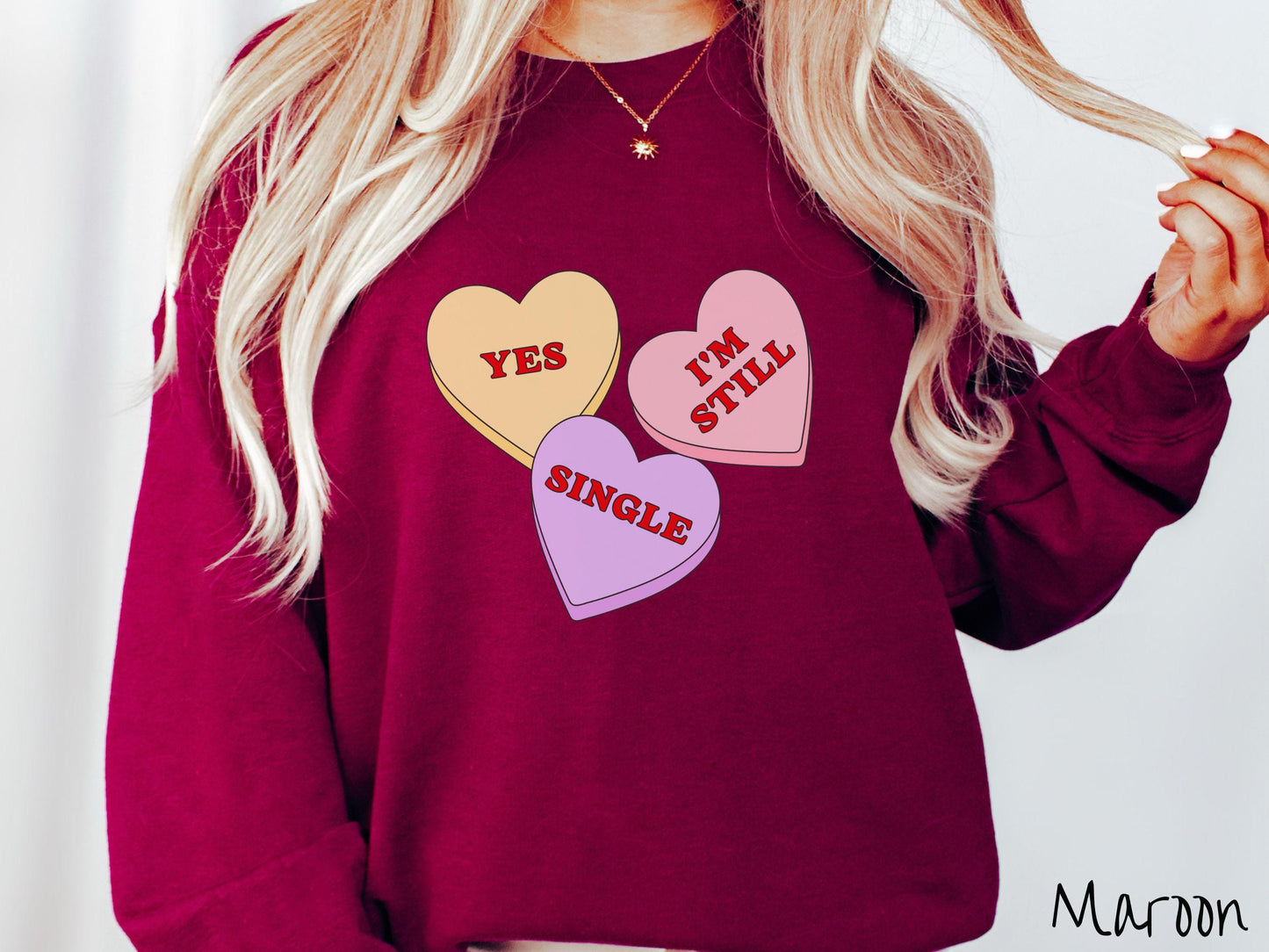 Make a bold statement this Valentine’s Day with this vintage Gildan sweatshirt featuring three vibrant conversation hearts in yellow, red, and purple, the design showcasing the cheeky phrase “Yes, I’m Still Single” spread across the hearts.
