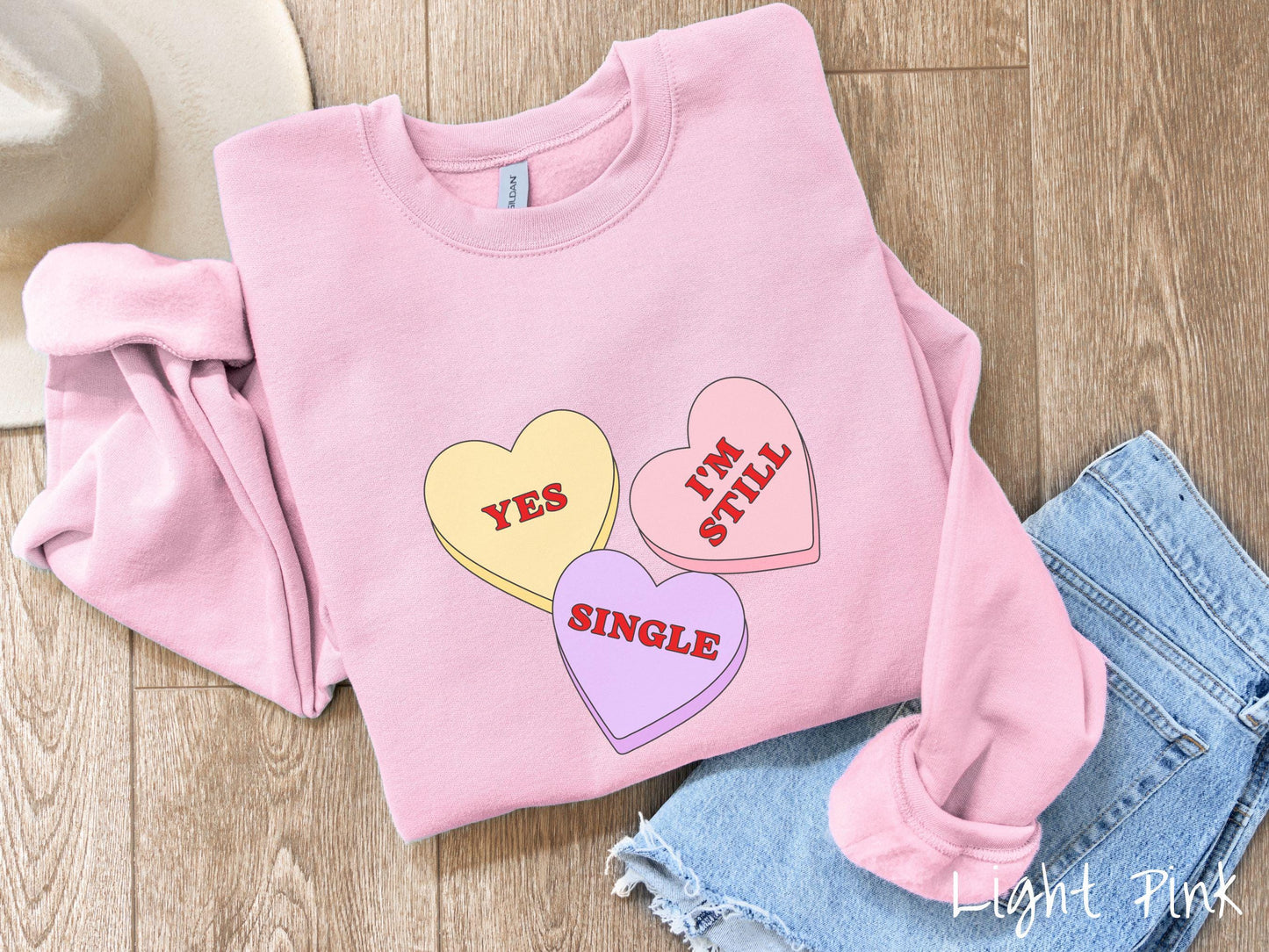 Make a bold statement this Valentine’s Day with this vintage Gildan sweatshirt featuring three vibrant conversation hearts in yellow, red, and purple, the design showcasing the cheeky phrase “Yes, I’m Still Single” spread across the hearts.