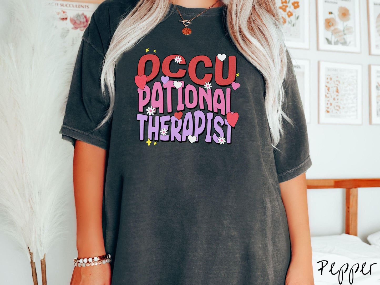 A stylish Comfort Colors t-shirt featuring the words "Occupational Therapist" arranged vertically in bold red, pink, and purple font, this design is enhanced with colorful hearts, flowers, and stars for a playful, uplifting touch.