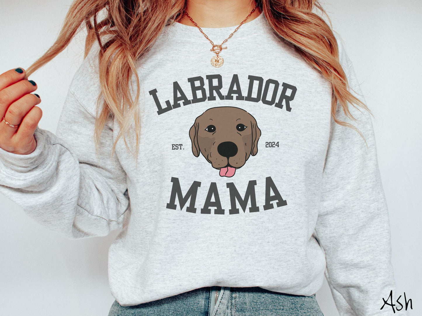 A vintage Gildan sweatshirt featuring bold block lettering that reads 'Labrador Mama.' At the center of the design, a playful chocolate Labrador with its tongue out steals the spotlight, framed by the stylish text 'EST. 2024.'