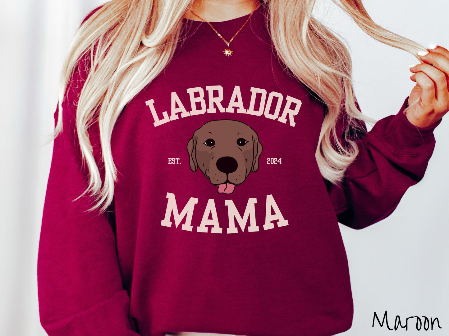 A vintage Gildan sweatshirt featuring bold block lettering that reads 'Labrador Mama.' At the center of the design, a playful chocolate Labrador with its tongue out steals the spotlight, framed by the stylish text 'EST. 2024.'