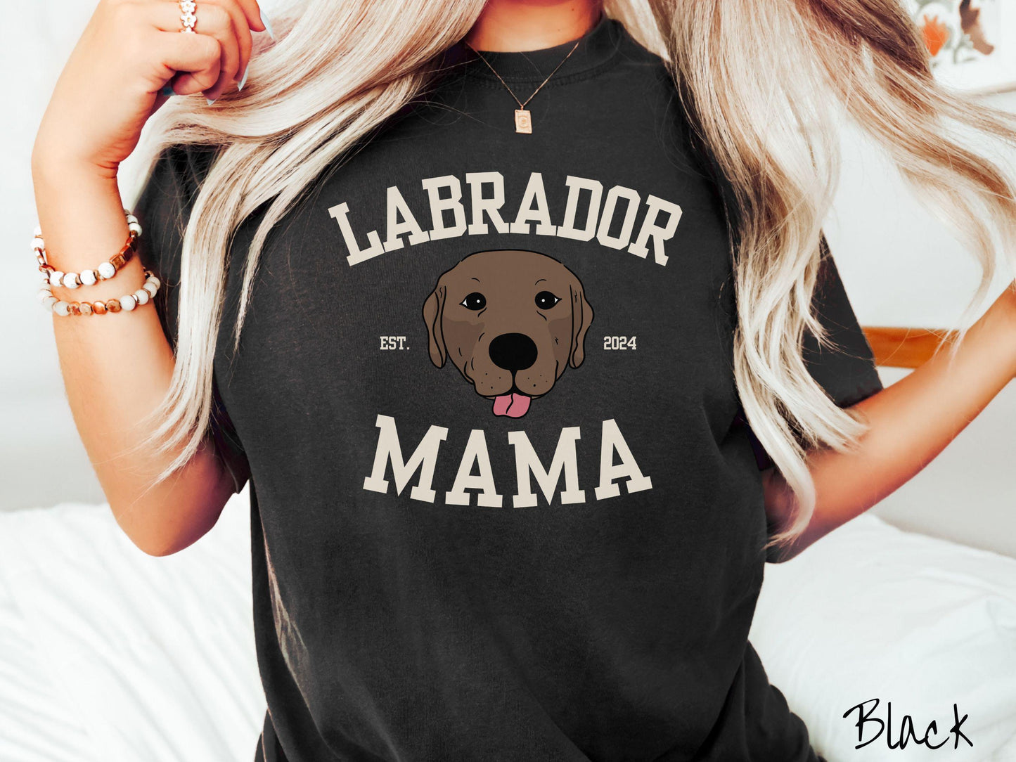 A vintage Comfort Colors t-shirt featuring bold block lettering that reads 'Labrador Mama.' At the center of the design, a playful chocolate Labrador with its tongue out steals the spotlight, framed by the stylish text 'EST. 2024.'