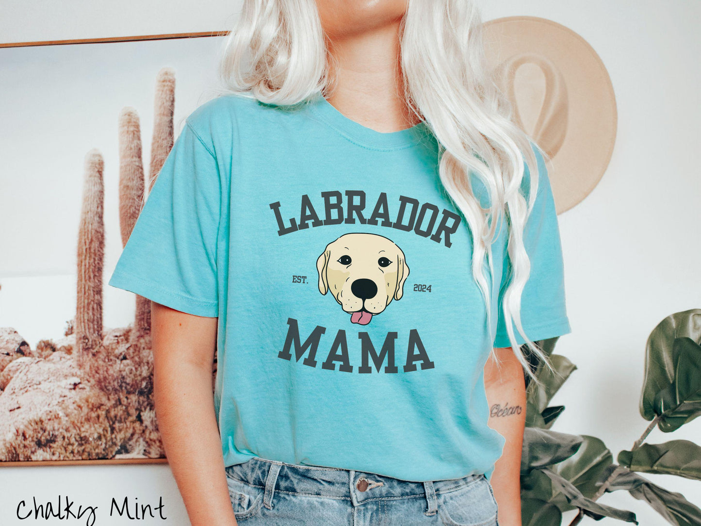 A vintage Comfort Colors t-shirt featuring bold block lettering that reads 'Labrador Mama.' At the center of the design, a playful yellow Labrador with its tongue out steals the spotlight, framed by the stylish text 'EST. 2024.'