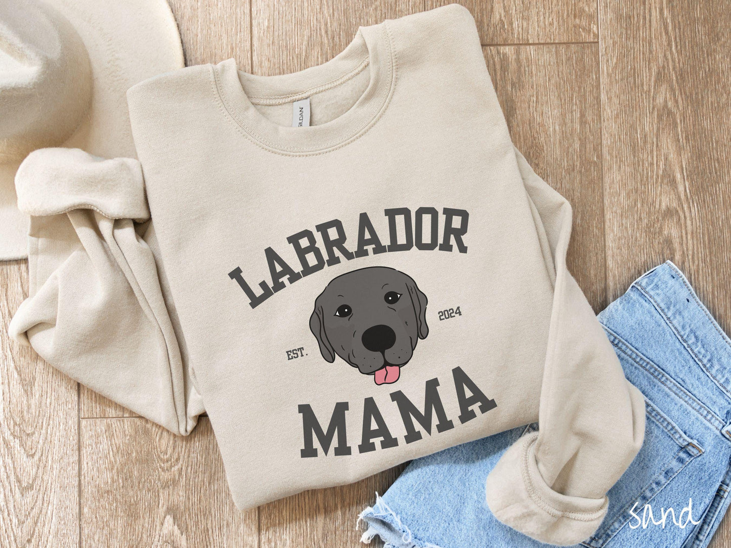 A vintage Gildan sweatshirt featuring bold block lettering that reads 'Labrador Mama.' At the center of the design, a playful black Labrador with its tongue out steals the spotlight, framed by the stylish text 'EST. 2024.'