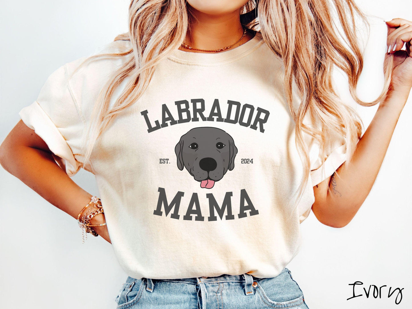 A vintage Comfort Colors t-shirt featuring bold block lettering that reads 'Labrador Mama.' At the center of the design, a playful black Labrador with its tongue out steals the spotlight, framed by the stylish text 'EST. 2024.'