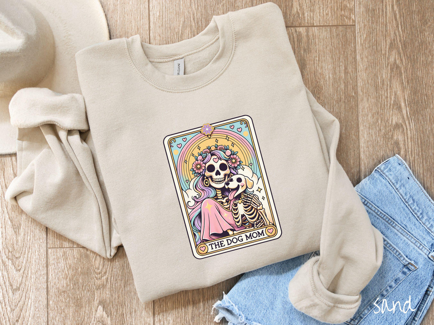 A vintage Gildan sweatshirt features a tarot card design with the text “The Dog Mom” along the bottom, framed by red hearts. Inside the tarot card is a female skeleton with flowing hair adorned with colorful flowers holding a skeleton dog.