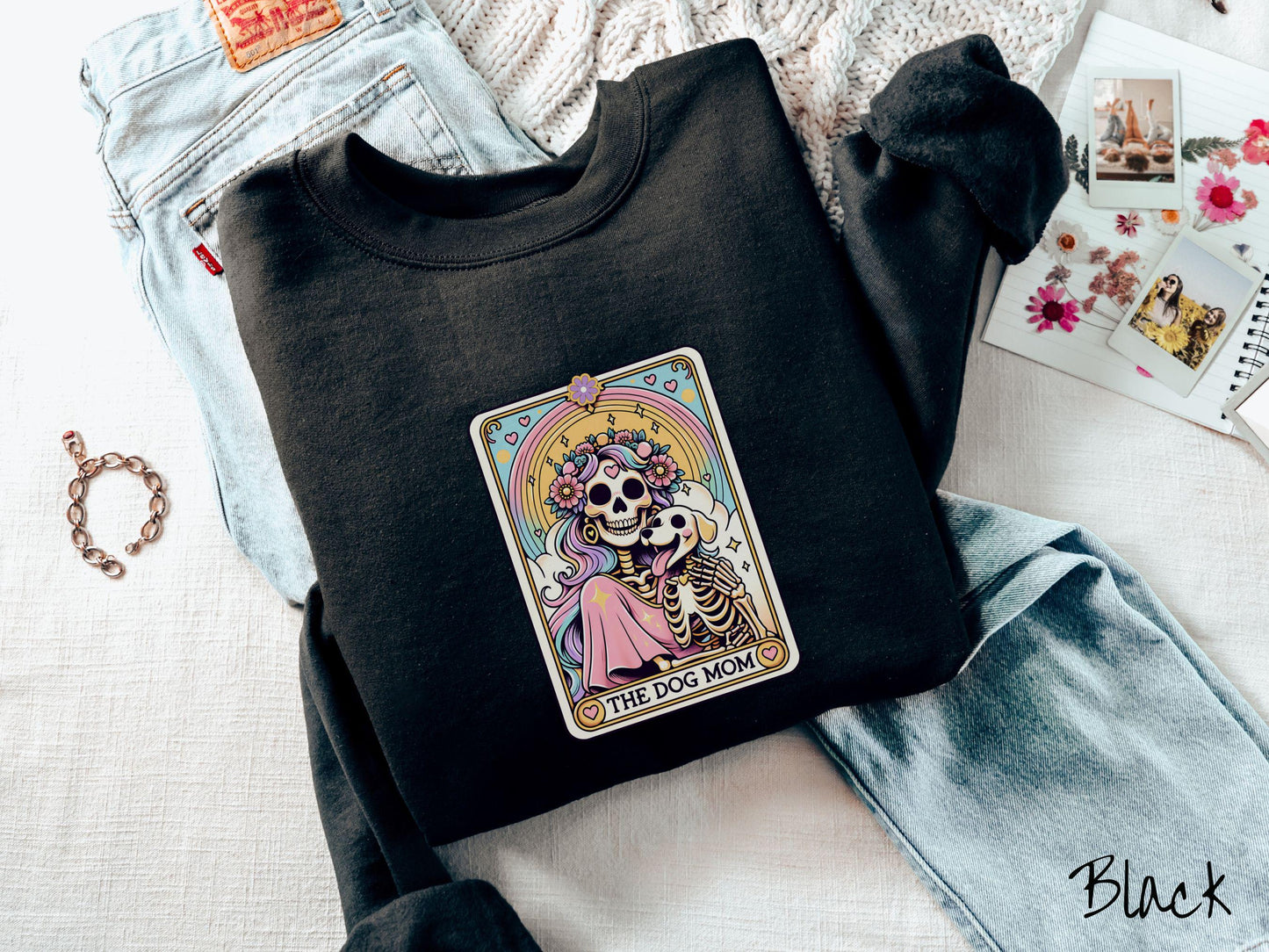 A vintage Gildan sweatshirt features a tarot card design with the text “The Dog Mom” along the bottom, framed by red hearts. Inside the tarot card is a female skeleton with flowing hair adorned with colorful flowers holding a skeleton dog.