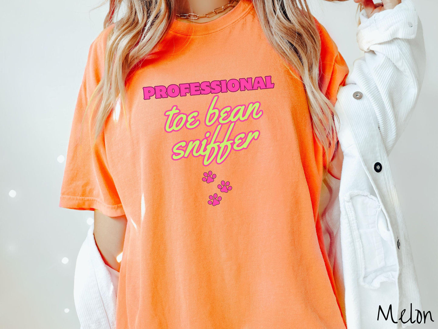 A vintage Comfort Colors t-shirt perfect for dog lovers who can’t resist those adorable toe beans! It features the funny text Professional Toe Bean Sniffer in bold pink and green fluorescent font, and below the text are three pink dog paw prints.