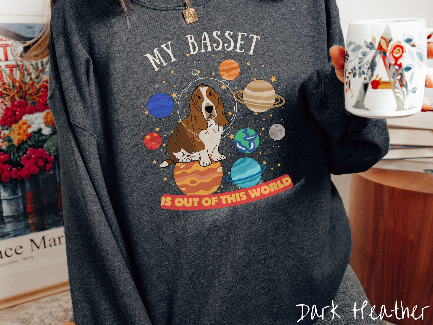 A vintage Gildan sweatshirt featuring the playful text 'My Basset is Out of This World'. The design showcases a basset hound sitting proudly atop Jupiter, surrounded by a vibrant solar system filled with colorful planets and twinkling stars.