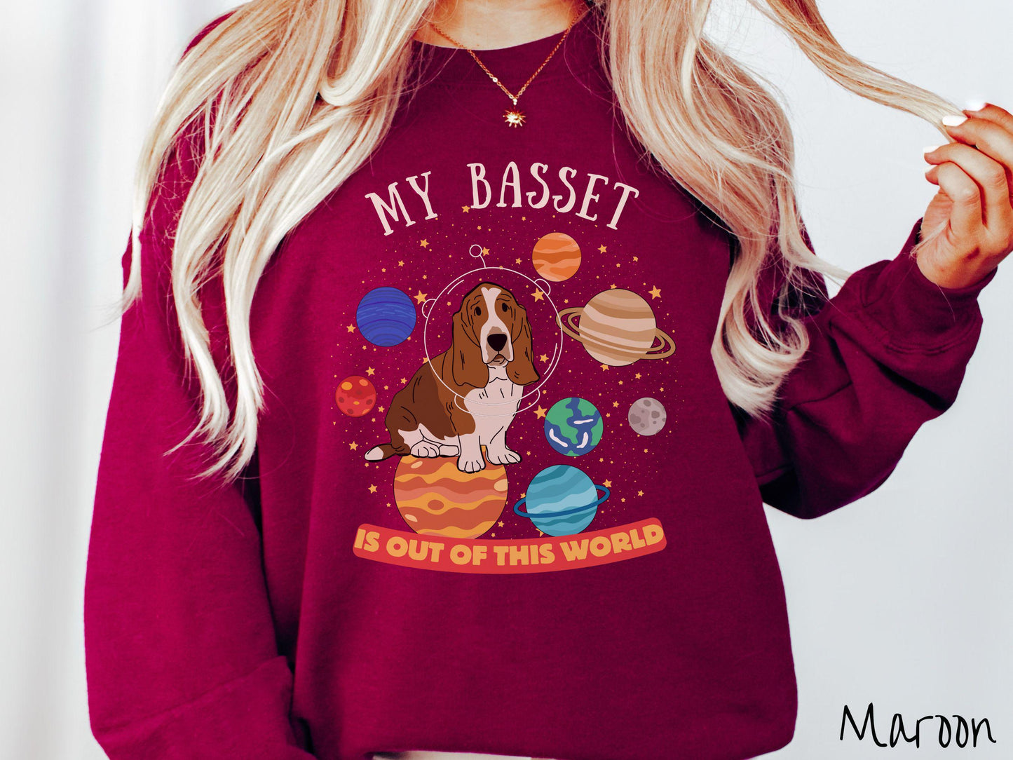A vintage Gildan sweatshirt featuring the playful text 'My Basset is Out of This World'. The design showcases a basset hound sitting proudly atop Jupiter, surrounded by a vibrant solar system filled with colorful planets and twinkling stars.