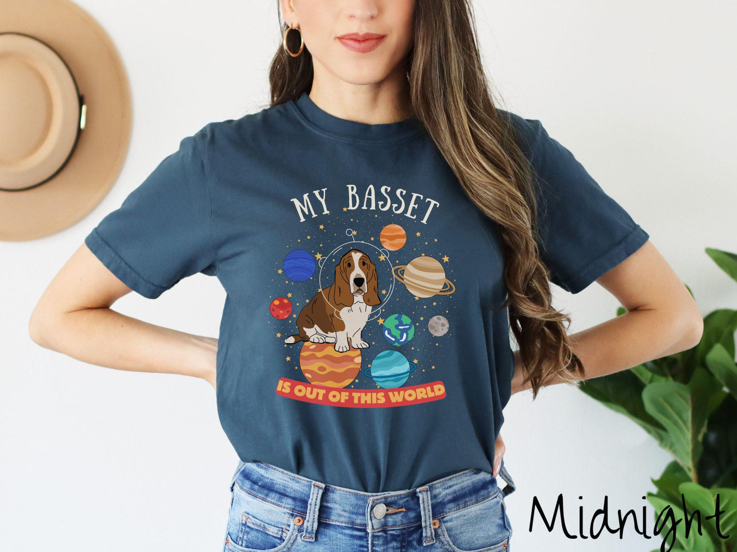 A vintage Comfort Colors t-shirt featuring the playful text 'My Basset is Out of This World'. The design showcases a basset hound sitting proudly atop Jupiter, surrounded by a vibrant solar system filled with colorful planets and twinkling stars.