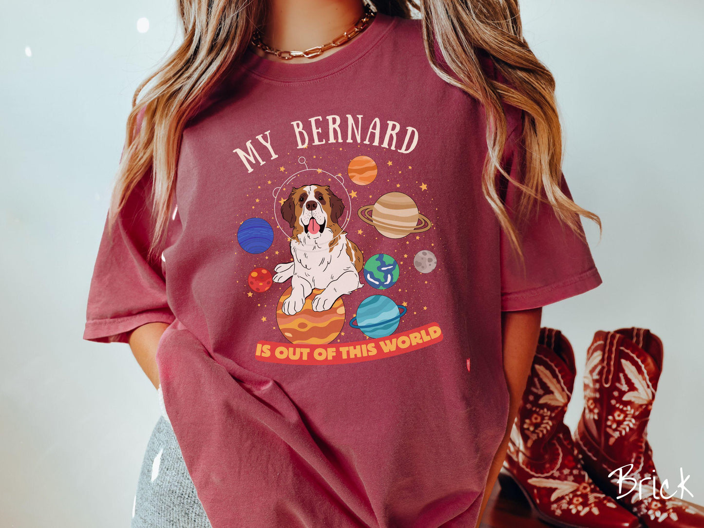 A vintage Comfort Colors t-shirt featuring the text 'My Bernard is Out of This World'. The design showcases an adorable St. Bernard sitting proudly atop Jupiter, surrounded by a vibrant solar system filled with colorful planets and twinkling stars.
